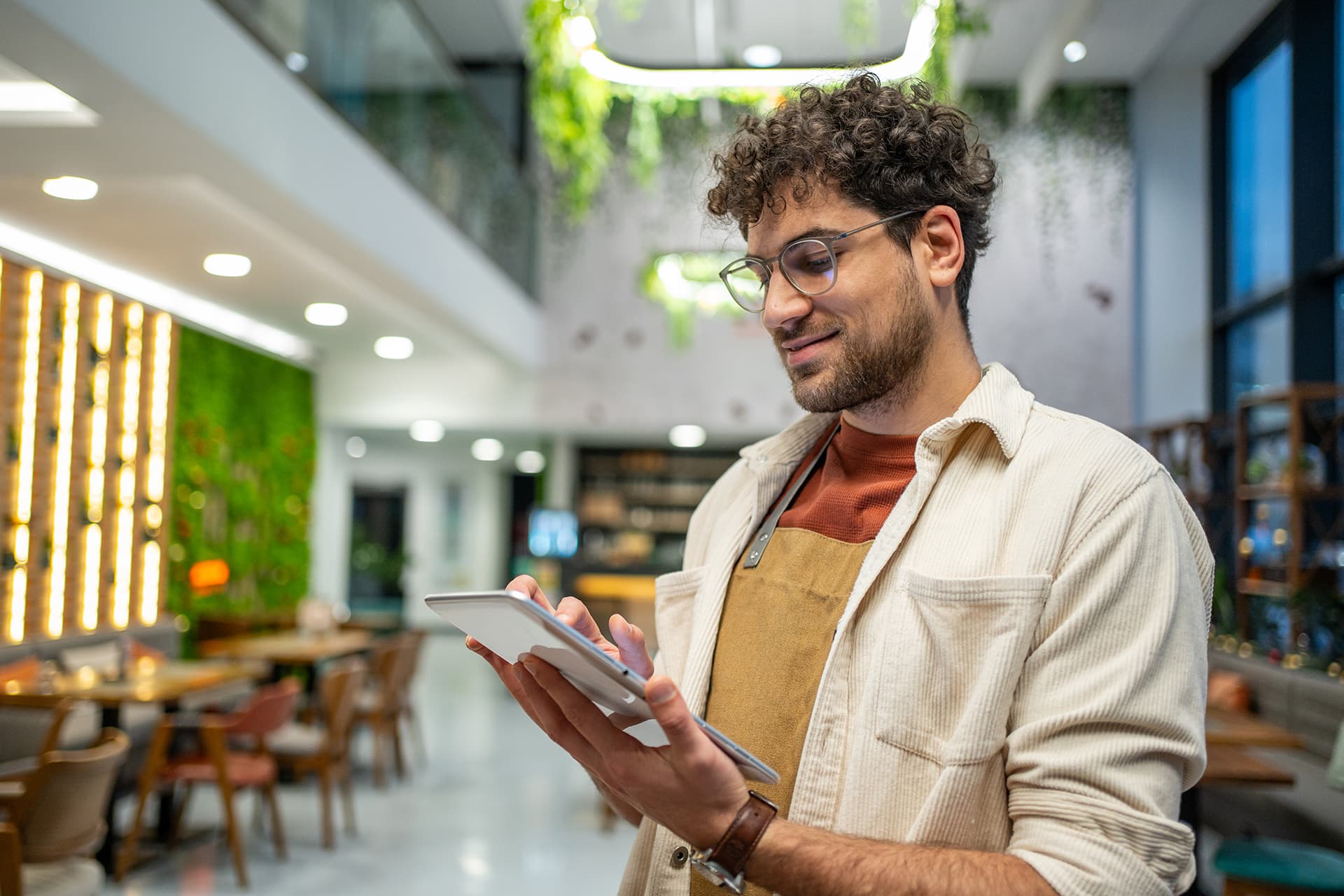 Mladý číšník s digitálním tabletem v kavárně