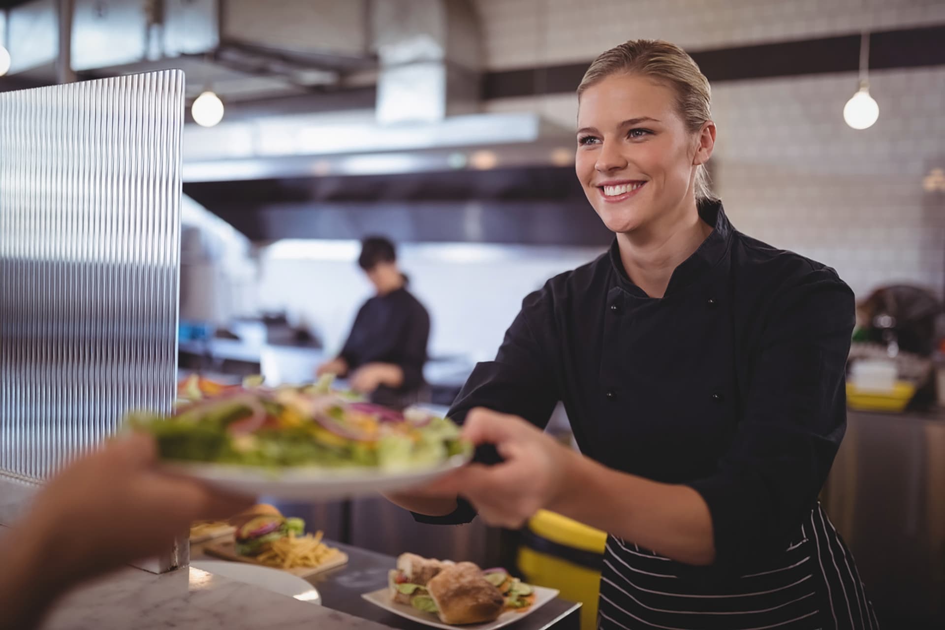 Junge Köchin übergibt griechischen Salat